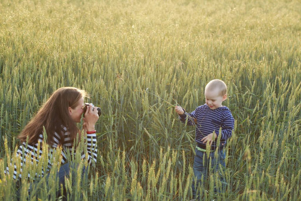 A mom takes a photo of her toddler in a wheat field